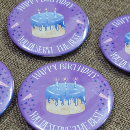 Set of purple buttons with birthday cake design and text on a textured surface