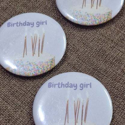 Three 'Birthday girl' buttons with toothpicks on a brown textured background